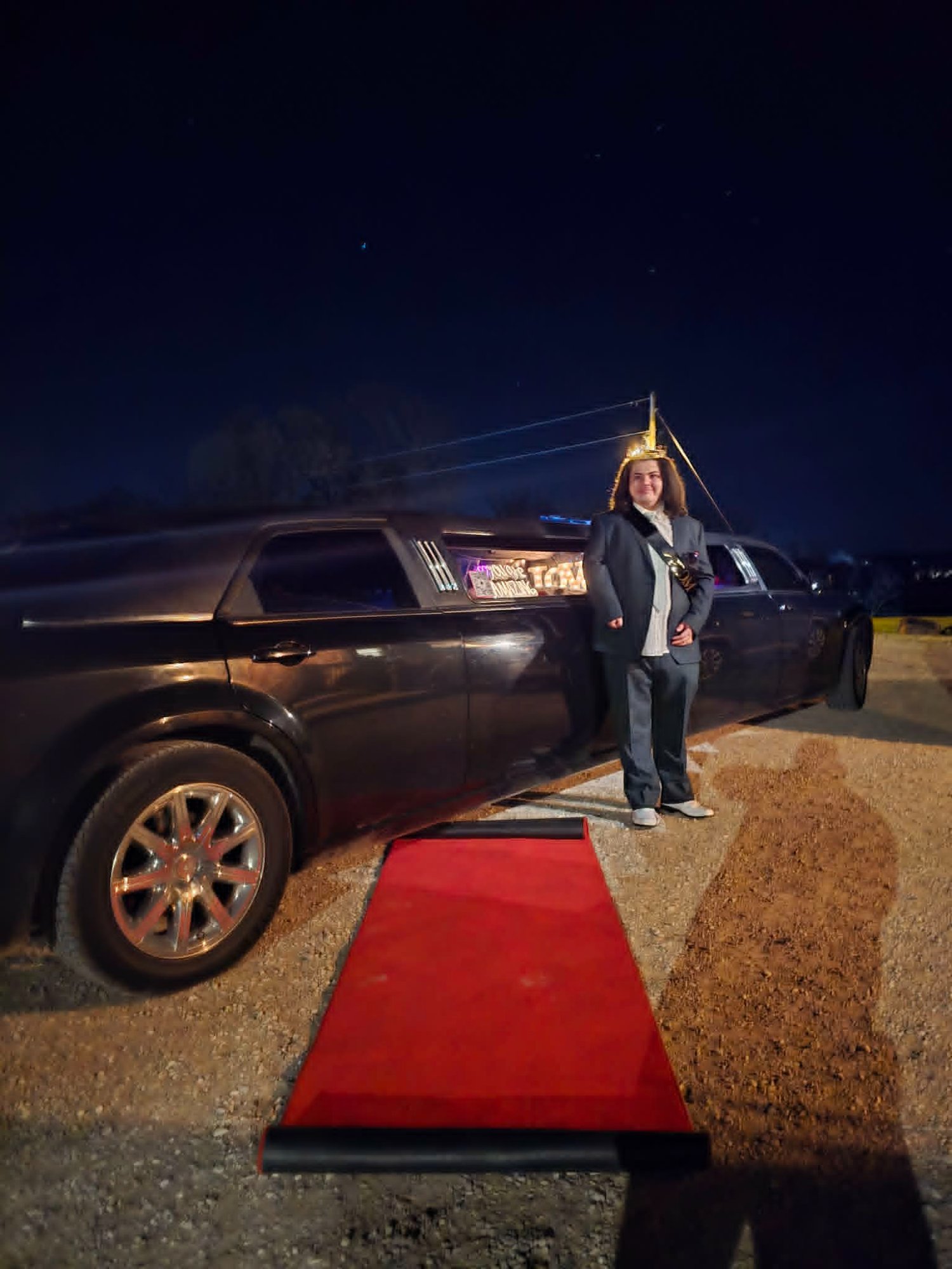 Mom wearing a crown standing on a red carpet next to The Executive stretch limo at night — Unique Rides Transportation Springfield MO parent prom night experience